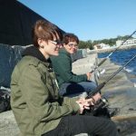Two cool people sit on the Victoria breakwater fishing in the sunshine
