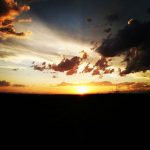The sun is a bright spot on the horizon of a dark land.