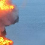 Smoke and fire rise up from a burn oil platform in the ocean.