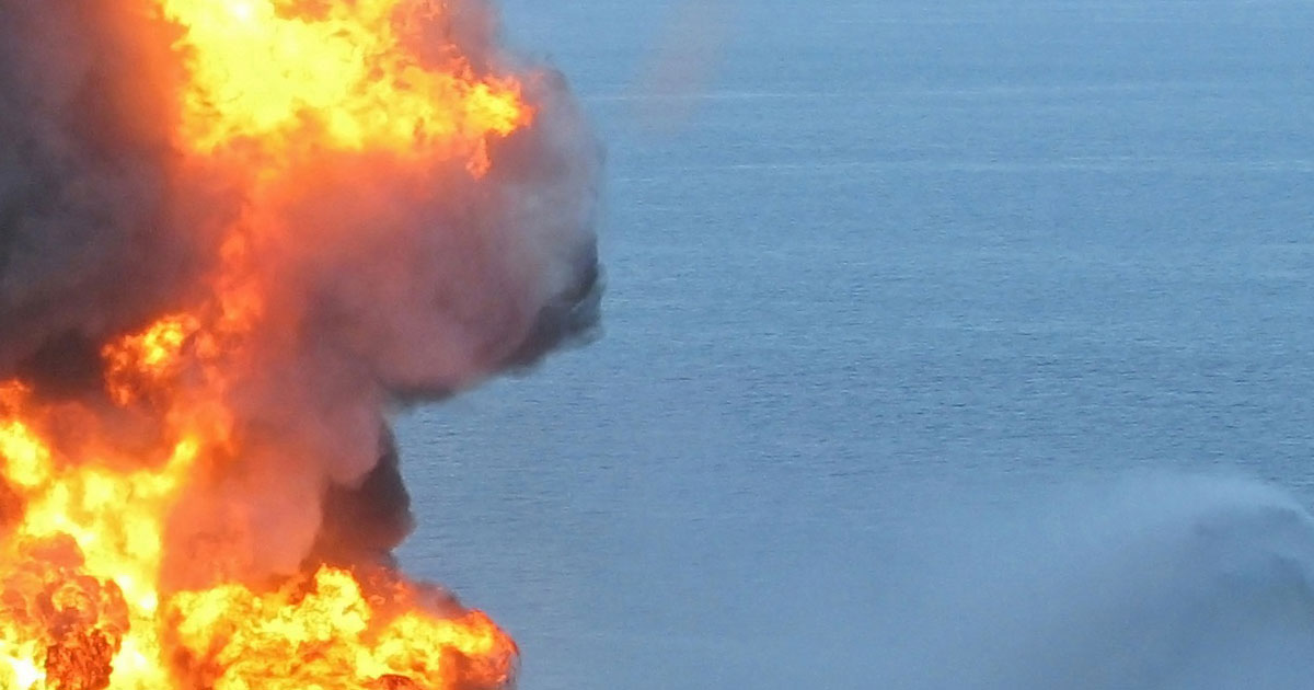 Smoke and fire rise up from a burn oil platform in the ocean.