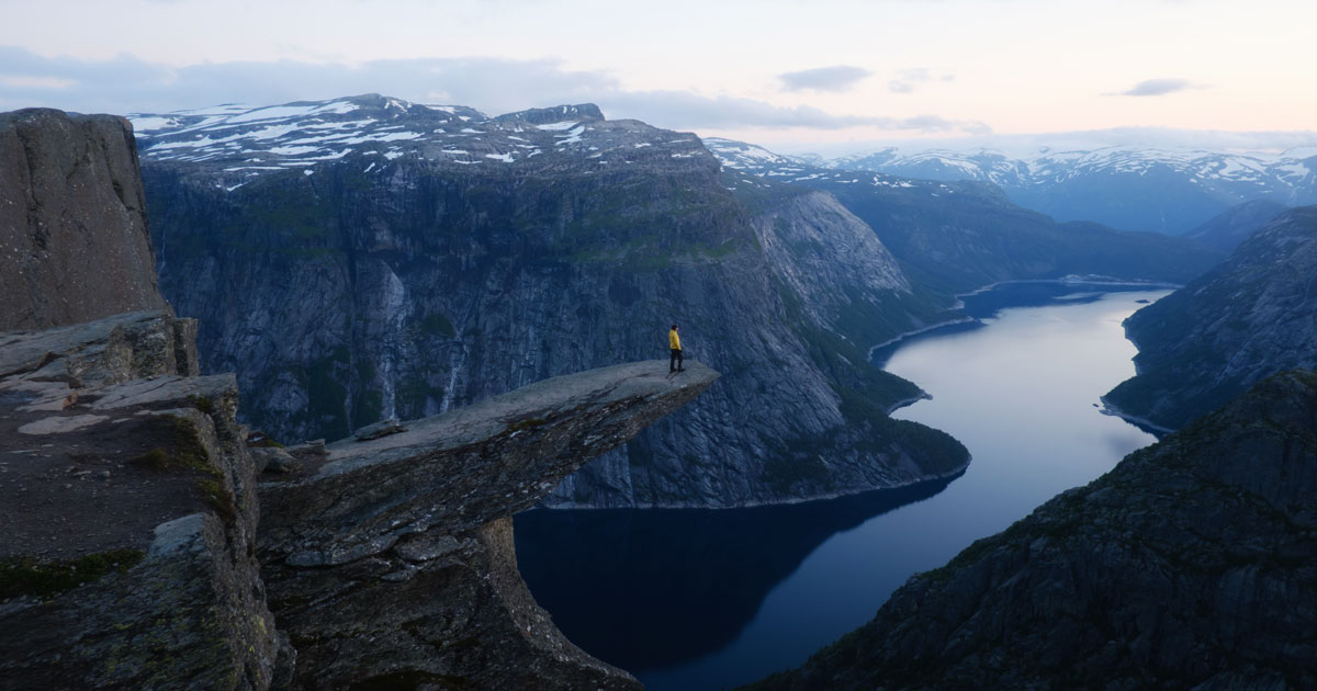 A small human stands on cliff overlooking a great divide in Norway.