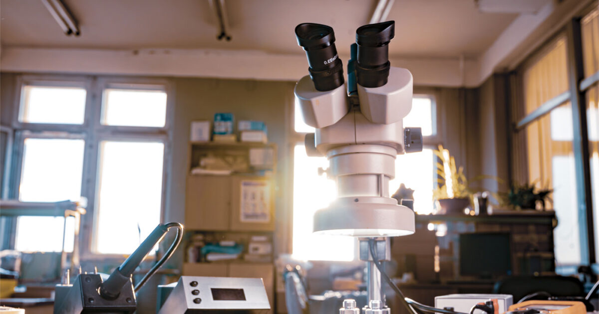 A microscope sits on a desktop of a busy lab.
